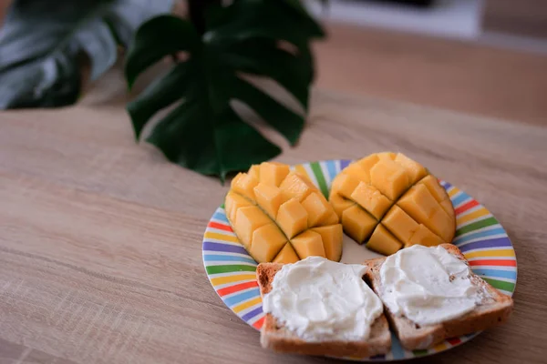 Ost sprids rostat bröd med mango skuren i kuber på en färgglad tallrik på ett träbord Royaltyfria Stockfoton