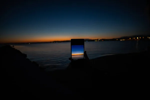 Mão humana segurando um telefone tirando uma foto de um pôr do sol — Fotografia de Stock