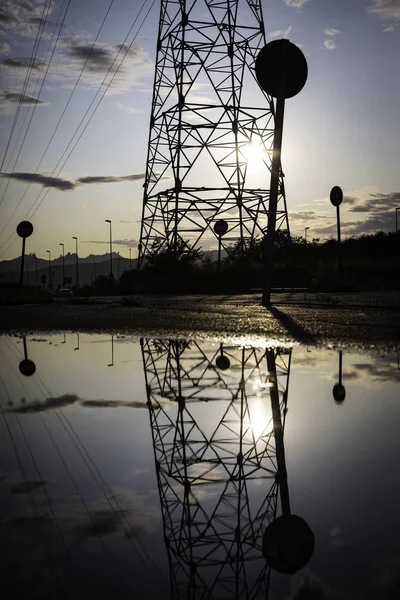 Reflection of a high voltage tower in a pond with the sky hidden behind on a cloudy evening