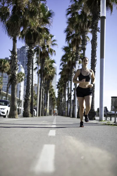 Beautiful woman in sport clothes running on the bike lane at the seafront in Barcelona (SPAIN)