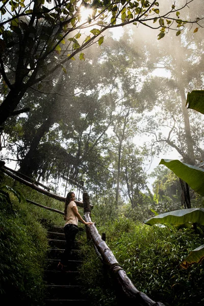 Beautiful woman on stairs on a foggy and wet rainforest path in