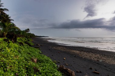Bali, Endonezya fırtınalı bir günde yeşil bitki örtüsü ile siyah kumlu plaj