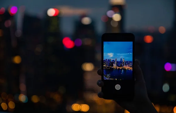 Woman hand holding a phone and taking a picture of the skyline v