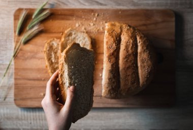 Elleri ev yapımı ve tahıllı ekmeği çiçeklerle süslenmiş ahşap bir masada tutan kadın.