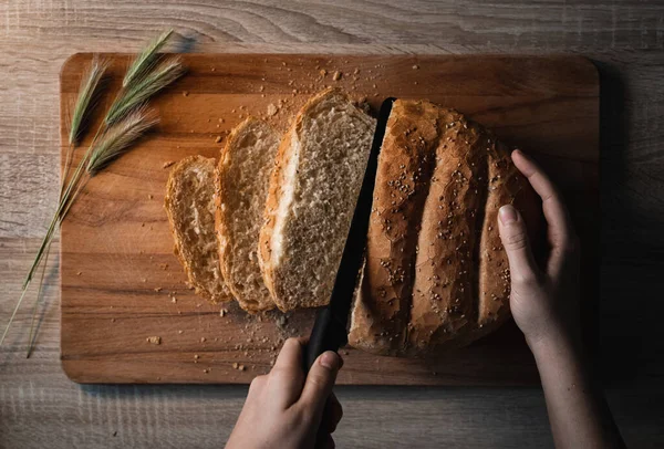 Woman hands cutting home made and baked grain bread on a wooden table with floral decoration and copy space