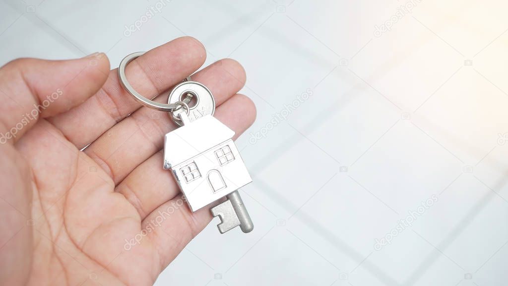 Male hand holding key with house trinket on light background, estate concept