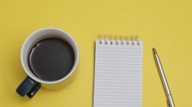 Bir fincan çay, not defteri ve kalem sarı arka plan, üst görünüm