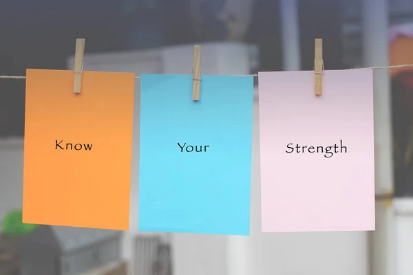 Word quotes of KNOW YOUR STRENGTH on sticky color papers hanging by a rope against blurred background. Vintage editing