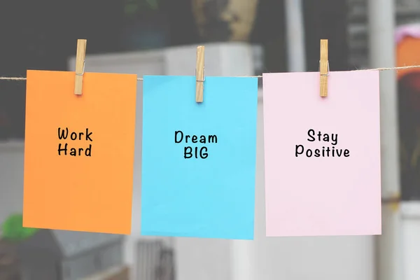 Word quotes of Work Hard, Dream Big, Stay Positive on sticky color papers hanging on rope against blurred background