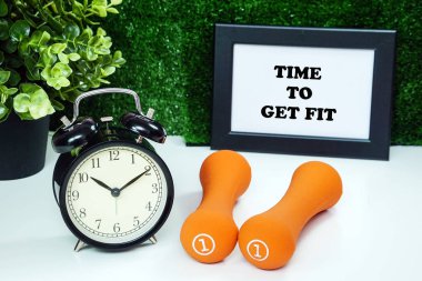 Çerçeve içinde ilham verici ifade ile beyaz masada çalar saat ve turuncu halter