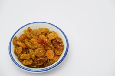 Beyaz arka planda beyaz kase üzerinde kuru üzüm yığını 