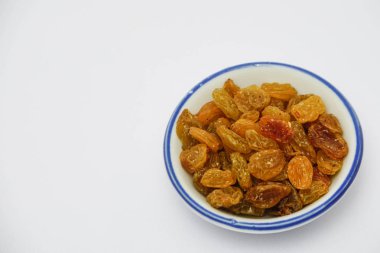 Beyaz arka planda beyaz kase üzerinde kuru üzüm yığını 