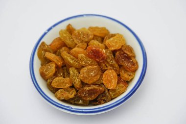 Beyaz arka planda beyaz kase üzerinde kuru üzüm yığını 