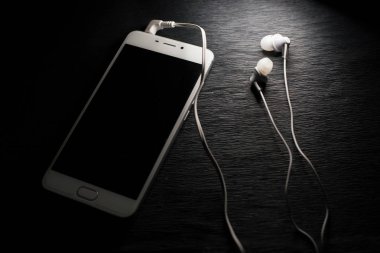 Siyah arka planda beyaz telefon ve kulaklıklar