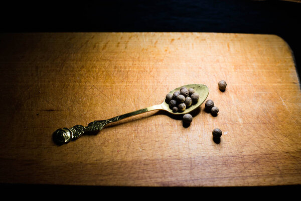 Black pepper on a spoon on a wooden board