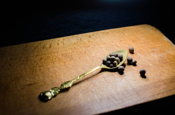Black pepper on a spoon on a wooden board