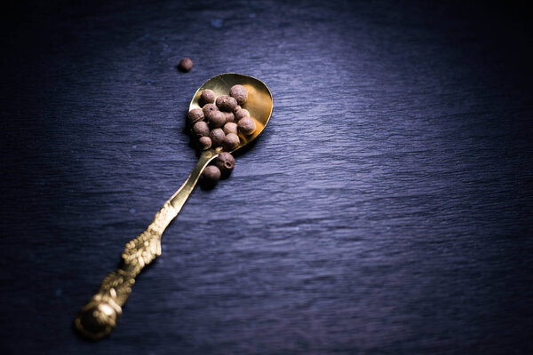 Black pepper on spoon on black background