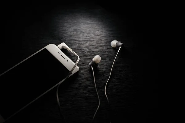 黒い背景に白い携帯電話とヘッドフォン — ストック写真