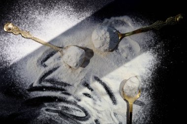 Siyah zemin üzerinde un olan altın kaşıklar.