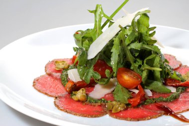 Beyaz tabakta domatesli, parmesanlı ve salamlı Arugula salatası..