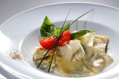 Parmesan peynirli Ravioli, otlar ve beyaz tabakta vişneli domates. İtalyan İtalyan mantı tortellini..