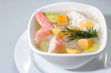 Yengeç etli çorba, pirinç eriştesi ve gri arka planda beyaz bir kasede yumurta..