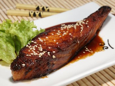 Bambu hasırında beyaz tabakta teriyaki soslu haşlanmış somon bifteği..