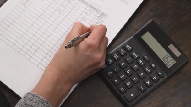 Woman accountant counts on a calculator and writes the result in a report. — Stock Video