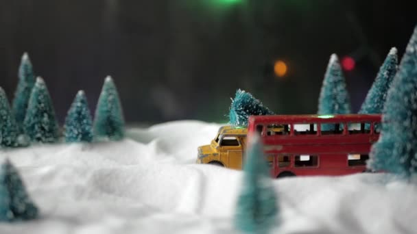 Een kleine speelgoed gele speelgoed auto met een kerstboom op het dak snelle ritten door een miniatuur speelgoed bos met sneeuwlaag en kerstbomen. — Stockvideo