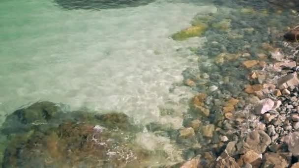 Ondas do mar a cair na costa rochosa. Areia e pedras podem ser vistas através da água — Vídeo de Stock