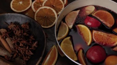 Sıcak şarap hazırlığı için. Kırmızı şarap, limonların, portakalların ve elmaların üstündeki tencerelere doluyor. Anise yıldızları ve tarçın çubukları ön plandaki kahverengi ahşap kasede. Üst görünümü kapat.