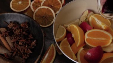 Sıcak şarap hazırlığı için. Limonların, portakalların, elmaların üstüne kırmızı şarap dök. Anise yıldızları ve tarçın çubukları ön plandaki kahverengi ahşap kasede. Üst görünümü kapat.
