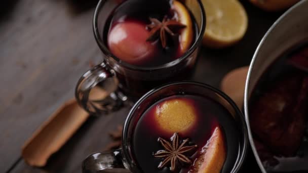 Top view of two glass mugs with mulled wine on brown wooden background. On top of vine surface anise star and slice of orange. Close up — Stock Video