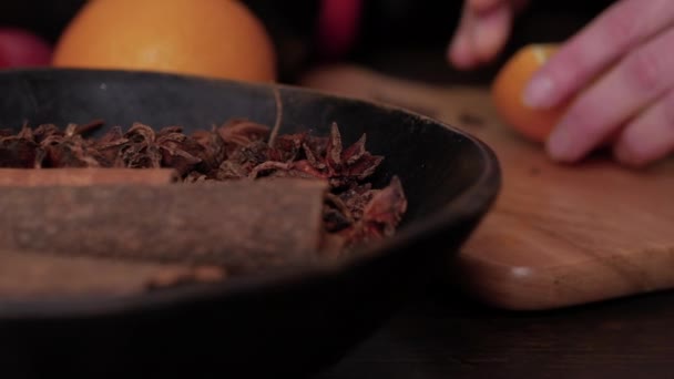 Preparation of mulled wine. Female hands cut orange on wooden cutting board. Anise stars and cinnamon sticks in brown wooden bowl in foreground. Close up slider shot. — ストック動画