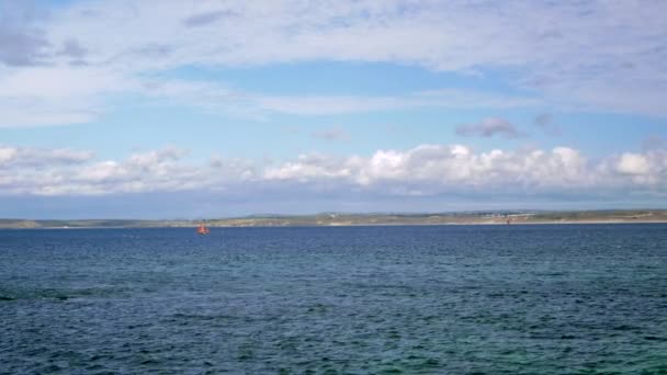 Un pequeño velero flota en el mar.Una costa rocosa es visible en la distancia . — Vídeo de stock