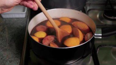 Sıcak şarap hazırlığı için. Şarap ocağının üstünde duran tencereli tencere kaynamaya başladı. Şarap buharı tencerenin üzerinde süzülüyor. Tahta kaşıkla kadın elleri şarabı karıştırır..