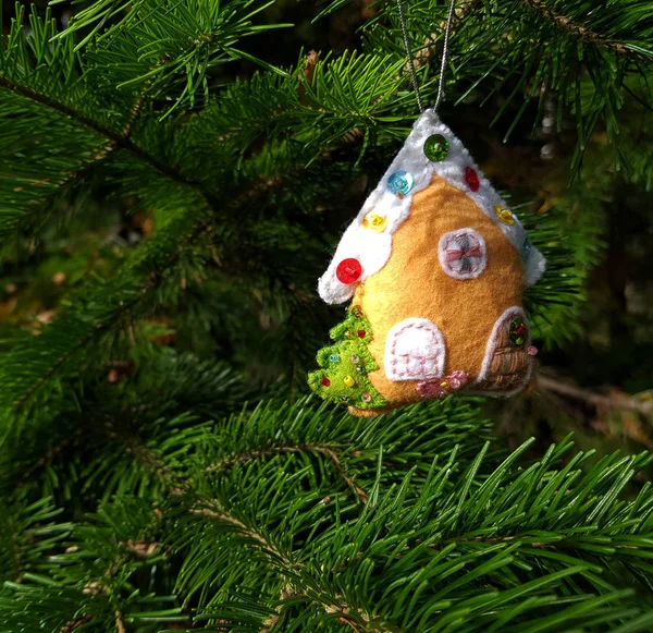 Christmas felt decoration on a spruce branch. Handmade bauble figurines of ginger house. Holiday background with a copy space.