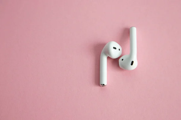 wireless white headphones without cord, lying next to each other on a pink background. Place for text