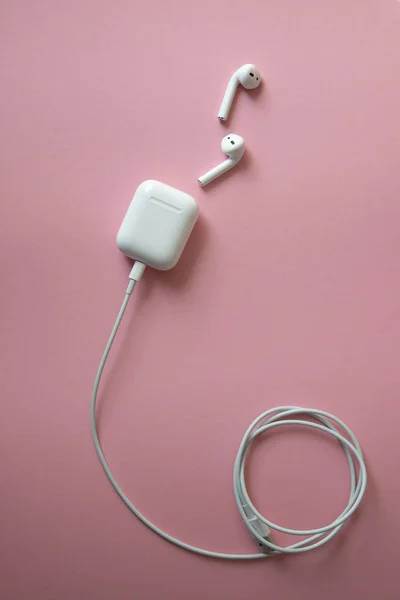 Casque blanc sans fil sur fond rose. Airpods. casque sans fil blanc avec un chargeur connecté à un câble d'alimentation enroulé en cercle — Photo