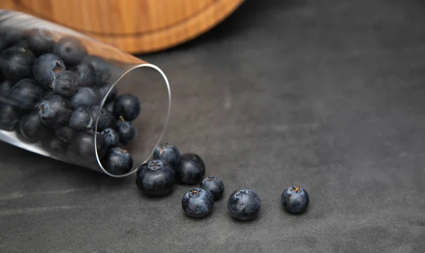 Fresh blueberries in a glass bowl. Delicious blueberries scattered from a glass cup. Gray background in the background is a wooden board. Place for tex