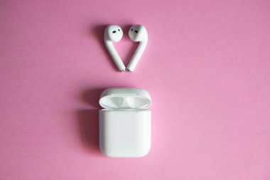 white wireless headphones lying over an open charger on a pink background. Place for text. Airpods. clipart