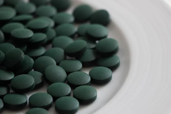 Green pills, spirulina tablets on a white plate — Stock Photo, Image