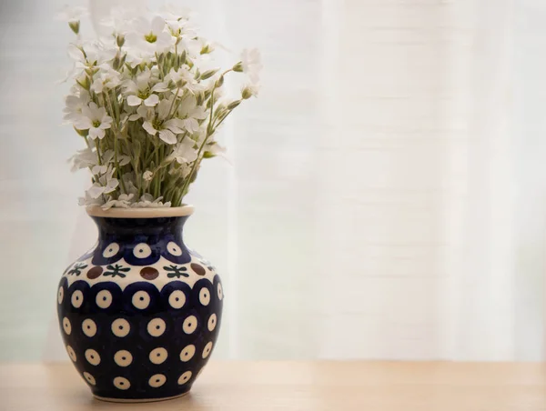 Petites fleurs blanches dans un vase. Un bouquet de fleurs yaskolki dans un vase en céramique gros plan. Fleurs dans un vase bleu avec un motif sur un fond blanc — Photo