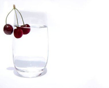 temiz içme suyu ve kenarında bir dal üzerinde üç kiraz ile bir cam bardak. Beyaz bir arka plan üzerinde su ve kiraz ile Cam. Kopyalama alanı