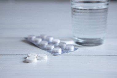 su ve üç beyaz hap, beyaz ahşap bir masa üzerinde vitamin ile cam. Masadaki ambalajdaki haplar. soğuk algınlığı tedavisi için geleneksel tıp
