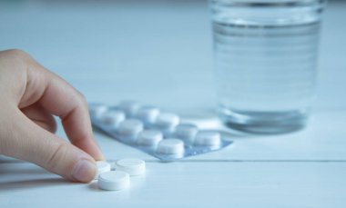 su ve üç beyaz hap, beyaz ahşap bir masa üzerinde vitamin ile cam. Masadaki ambalajdaki haplar. Parmaklar hap tutuyor. soğuk algınlığı tedavisi için geleneksel tıp