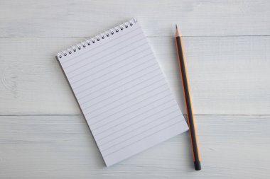 Cetveldeki not defteri boş bir sayfada açık ve yakınlarda bir kalem bulunmaktadır. Defter ve kalem beyaz ahşap bir masa üzerinde yalan