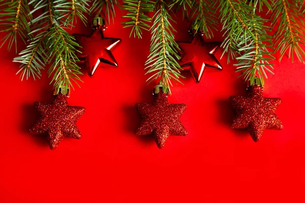 Vánoční koncept. jedlové větve a vánoční ozdoby, hračky, červené hvězdy na červeném pozadí — Stock fotografie