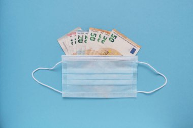 Yüksek ilaç ve tıbbi ekipman maliyeti kavramı. Mavi arka planda Euro parası olan tıbbi maske. Metin için yer.