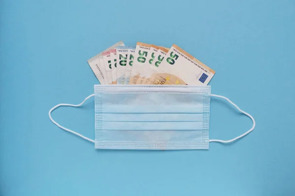 The concept of the high cost of drugs and medical equipment. Medical mask with euro money on a blue background. Place for text.